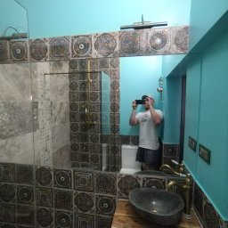 Kacper Czop - Wykończona łazienka z turkusowymi ścianami i dekoracyjnymi płytkami. Umywalka z kamienia i bateria w stylu retro. W lustrze odbija się osoba robiąca zdjęcie.