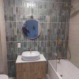 Kacper Czop - Nowoczesna łazienka z umywalką nablatową, baterią w kolorze złota i zielonymi płytkami ułożonymi pionowo. W lustrze odbija się osoba robiąca zdjęcie.