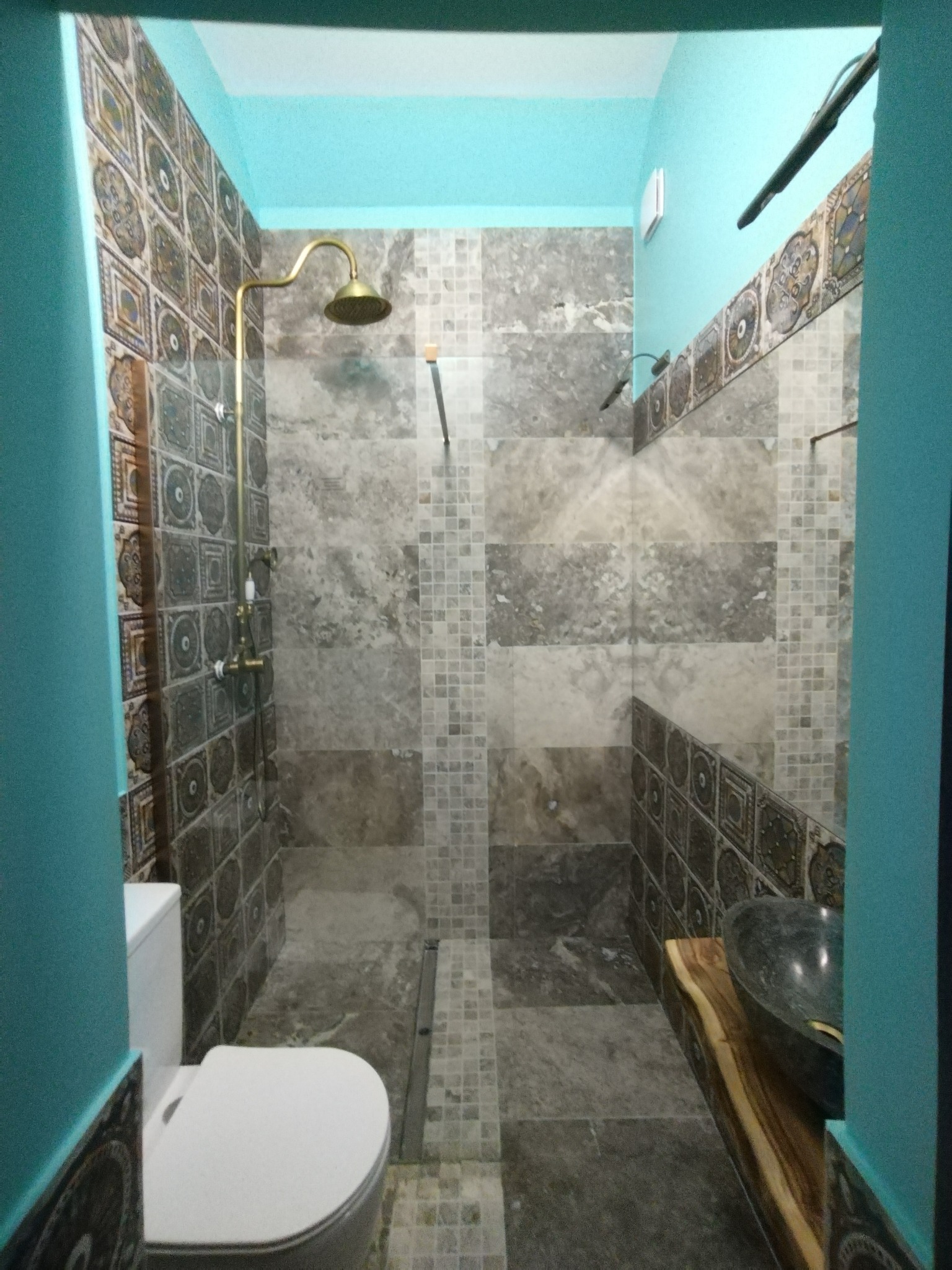 Wykończona łazienka z kabiną prysznicową typu walk-in, mozaiką i złotą armaturą. Umywalka nablatowa na blacie z naturalnego drewna. Turkusowe ściany.