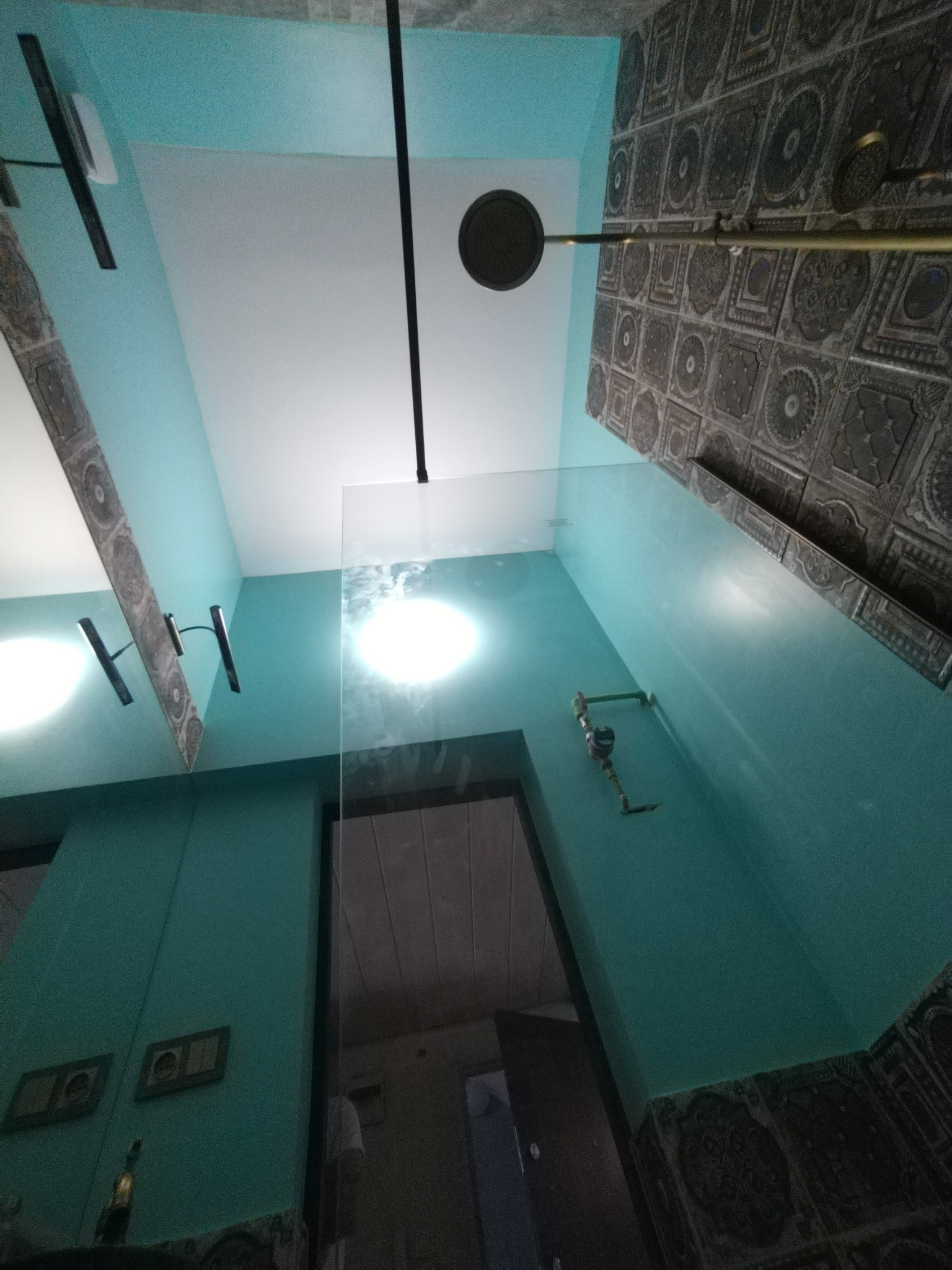 Wykończona łazienka z turkusowymi ścianami, dekoracyjnymi płytkami i szklanym panelem prysznicowym. Widok z dołu, podkreślający oświetlenie i detale wykończenia.