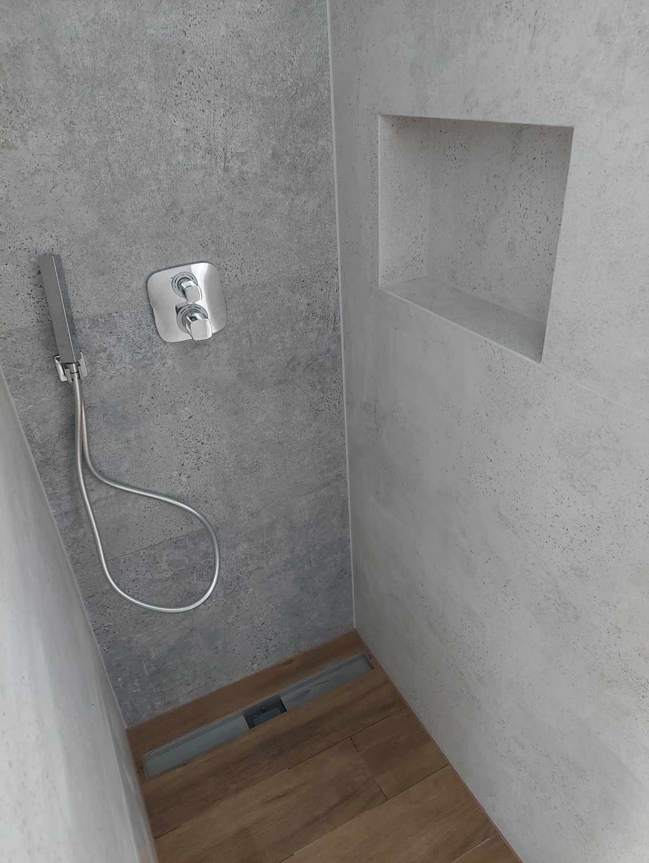 Nowoczesna kabina prysznicowa z szarą, teksturowaną ścianą i drewnopodobną podłogą w Kwidzynie. Wnęka w ścianie i minimalistyczna armatura.