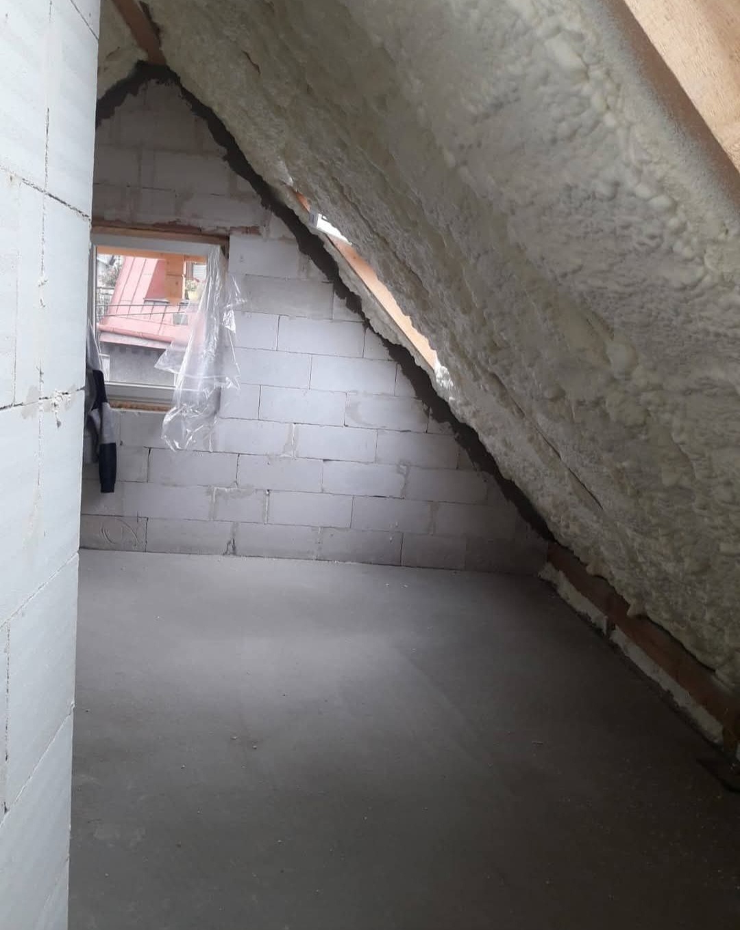 Poddasze po ociepleniu pianką PUR, widoczne białe bloczki i okno. Ocieplona skośna ściana i fragment podłogi. Detal izolacji poddasza.