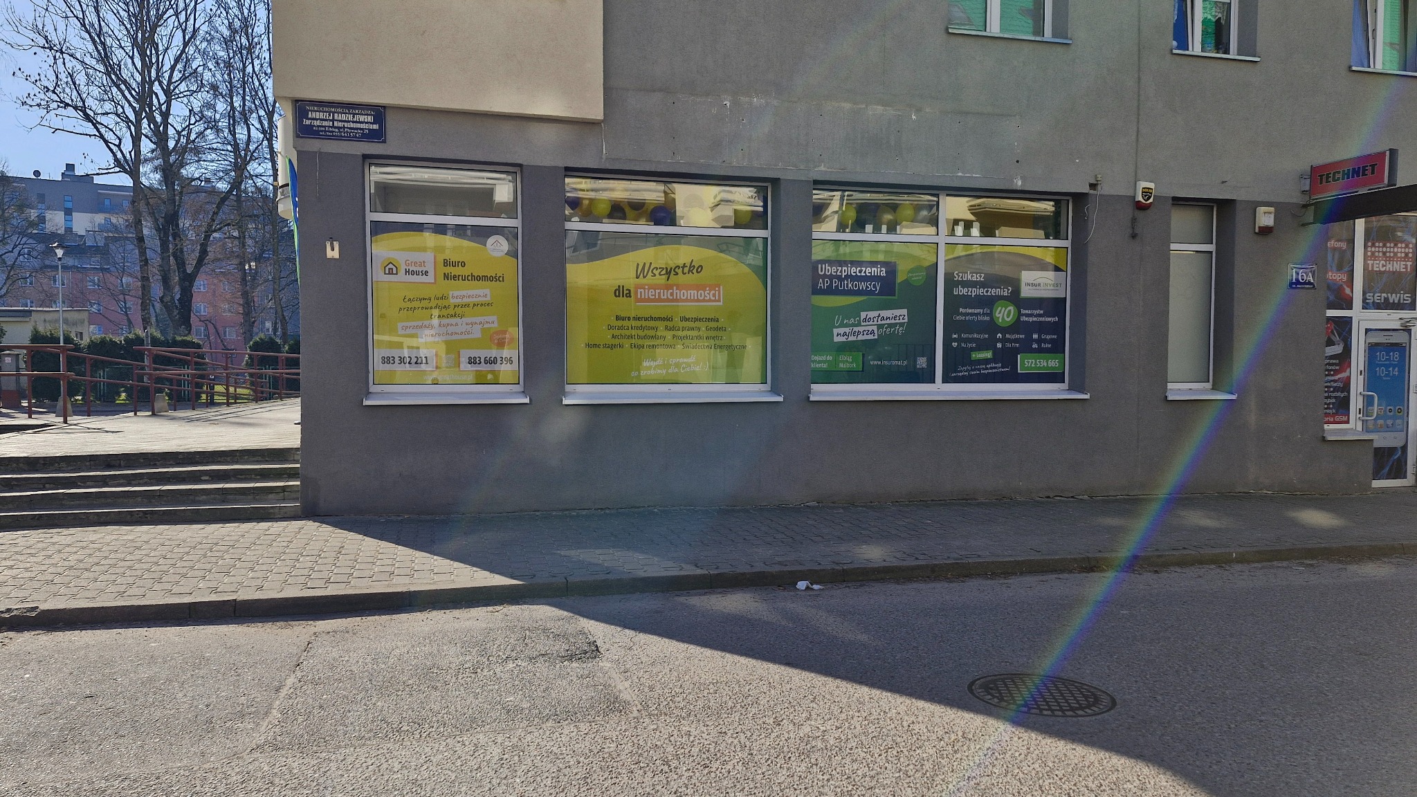 Fasada biura nieruchomości z oknami oklejonymi reklamami usług: sprzedaż, kupno, kredyty, ubezpieczenia, projektowanie wnętrz, home staging, geodeta, architekt, radca prawny.