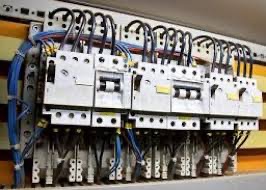 Rozdzielnia elektryczna z bezpiecznikami, widoczne kable i oznaczenia, wnętrze szafki, ujęcie z bliska, lekki kąt z góry.