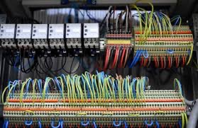 Rozbudowana instalacja elektryczna: liczne przewody w różnych kolorach podłączone do listew zaciskowych i modułów sterujących wewnątrz szafy elektrycznej.