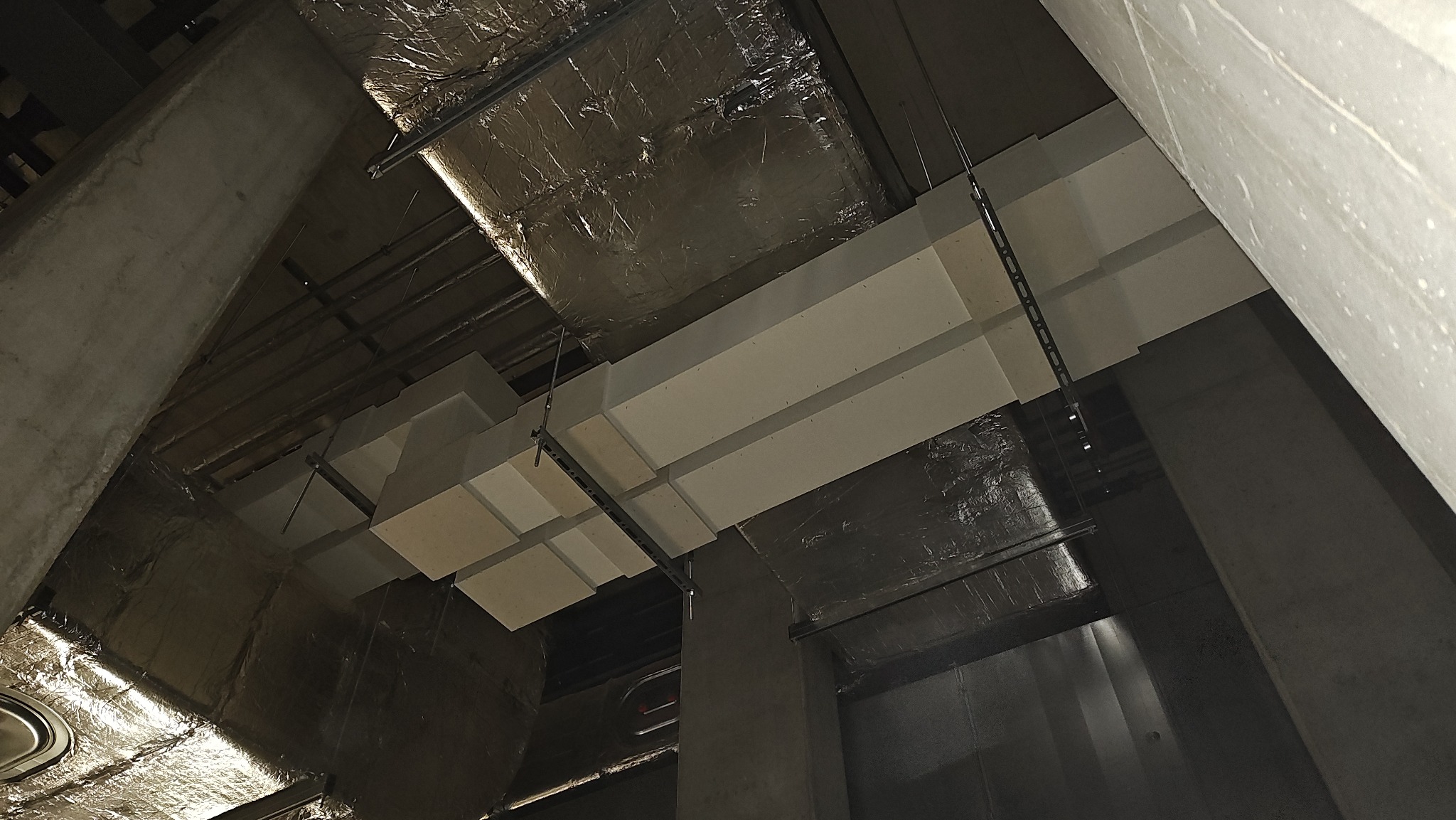 Instalacja sufitowa z elementami izolacyjnymi i konstrukcją wsporczą, widok z dołu, surowe wykończenie, szara kolorystyka.