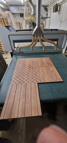 Frezowana płyta drewniana z dekoracyjnym wzorem na stole frezarki CNC, z widocznymi elementami systemu odsysania pyłu.