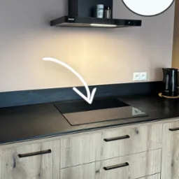 Kuchnia z płytą indukcyjną, podłączoną przez elektryka. Strzałka wskazuje na płytę. Widoczny okap i gniazdka elektryczne. Ujęcie z bliska, bez osób.