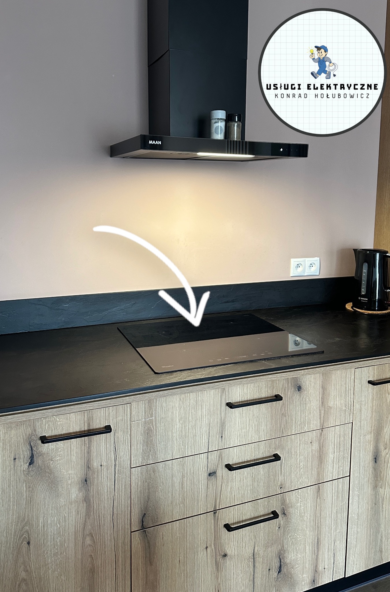 Kuchnia z płytą indukcyjną, podłączoną przez elektryka. Strzałka wskazuje na płytę. Widoczny okap i gniazdka elektryczne. Ujęcie z bliska, bez osób.