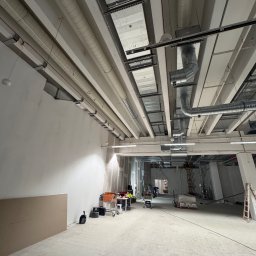 Tilda AP - Wnętrze w trakcie instalacji wentylacji: widoczne rury wentylacyjne pod sufitem, narzędzia i materiały budowlane, surowy stan wykończenia pomieszczenia.