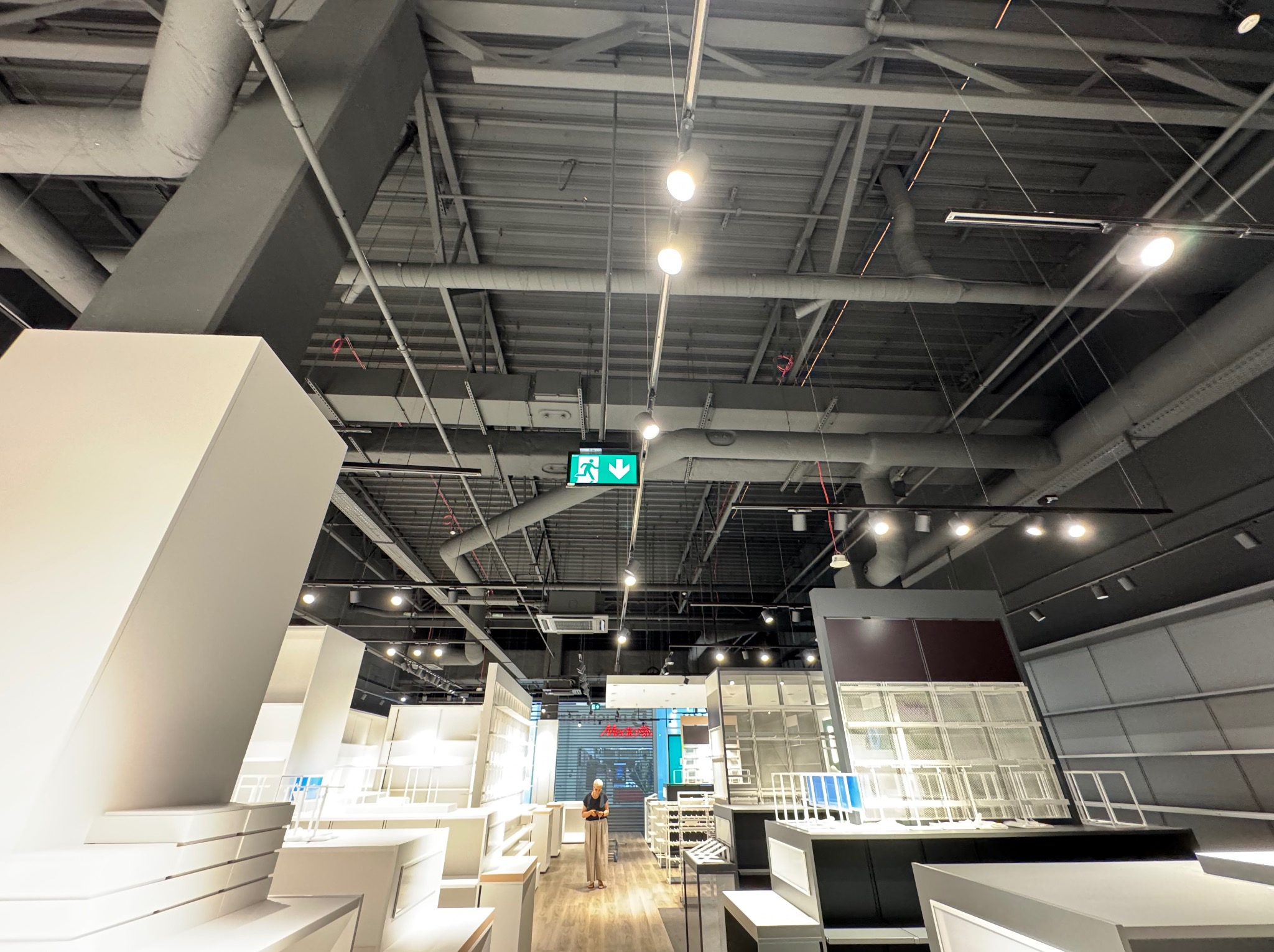 Sufit w obiekcie komercyjnym z widocznymi instalacjami wentylacyjnymi, rurami i oświetleniem. Na pierwszym planie wyposażenie sklepu.