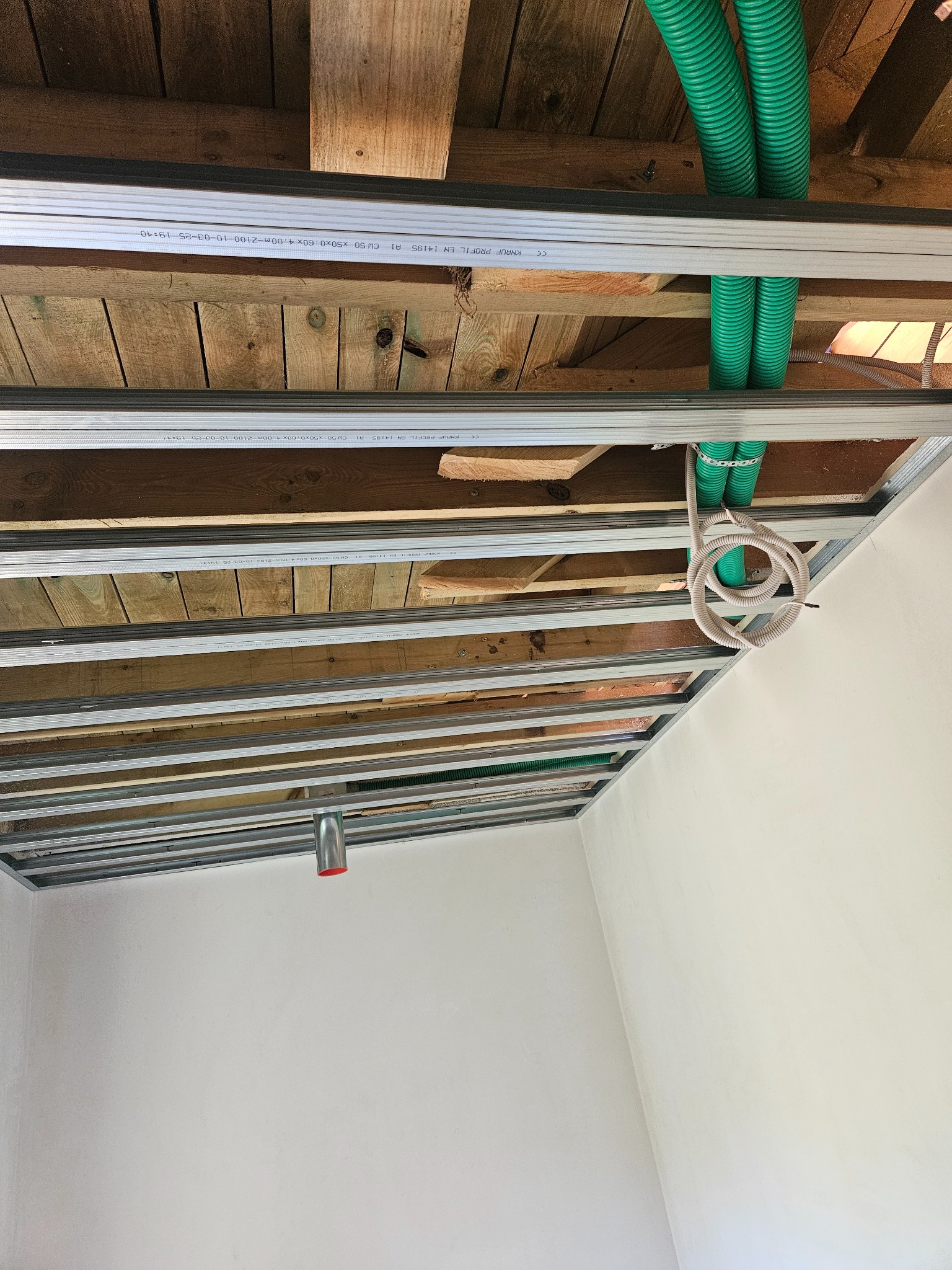 Montaż sufitu podwieszanego z płyt karton-gips w Jaworznie. Widoczne profile metalowe, zielone rury instalacyjne i drewniana konstrukcja stropu.