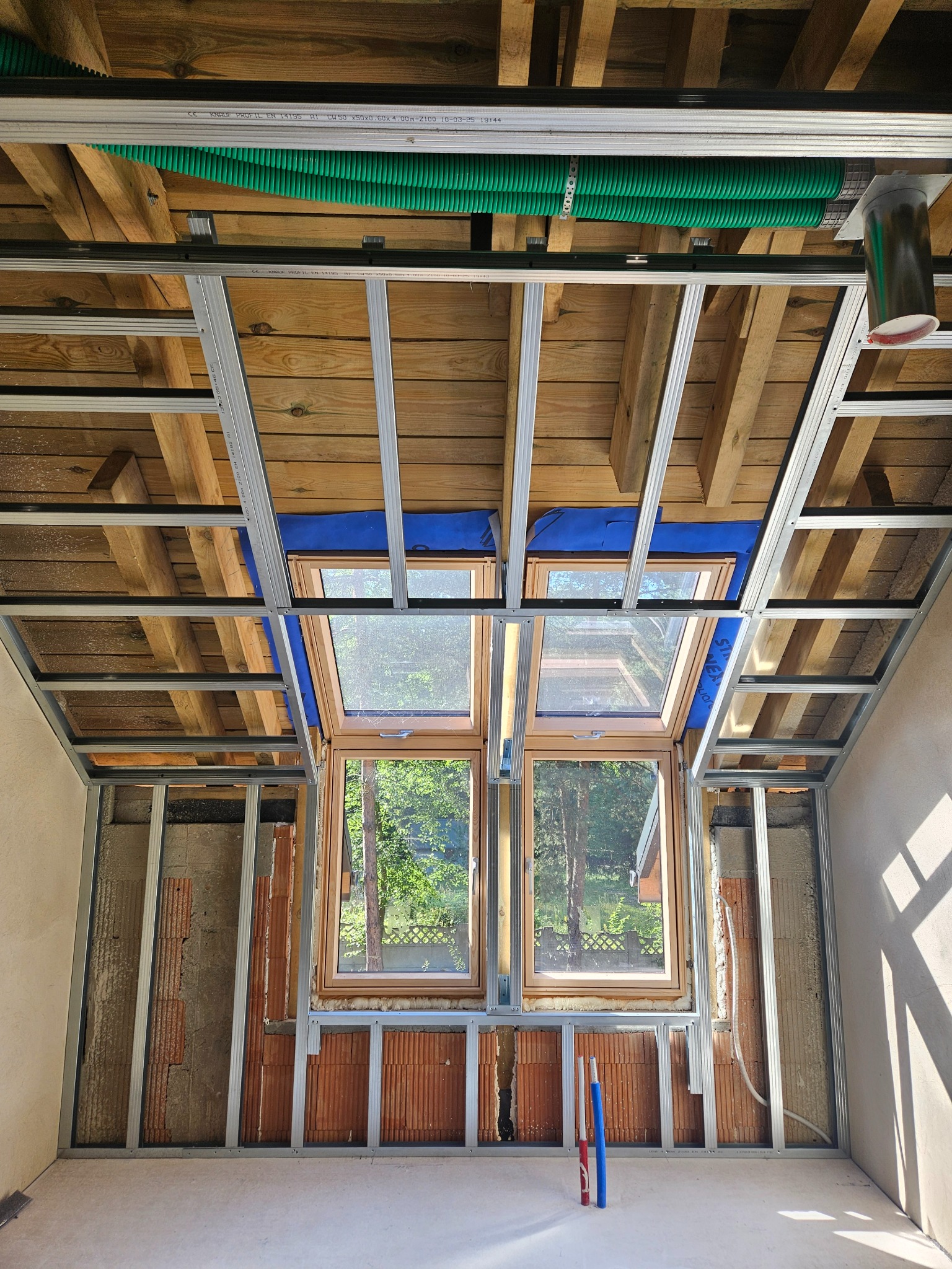 Szkielet sufitu i ścian z profili metalowych, okna dachowe, widoczne instalacje elektryczne w rurach. Wnętrze w trakcie wykańczania, surowy stan.