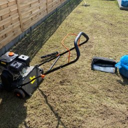 ECO SKILS - Wertykulator spalinowy na trawniku po zabiegu. Widoczny drewniany płot, grabie i worki na trawę. Aeracja trawnika w słoneczny dzień.