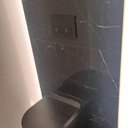 Paweł Kobyliński - Elegancka, czarna toaleta podwieszana na tle ściany wyłożonej czarnym marmurem z białymi żyłami. Minimalistyczny design, oświetlenie LED po bokach.