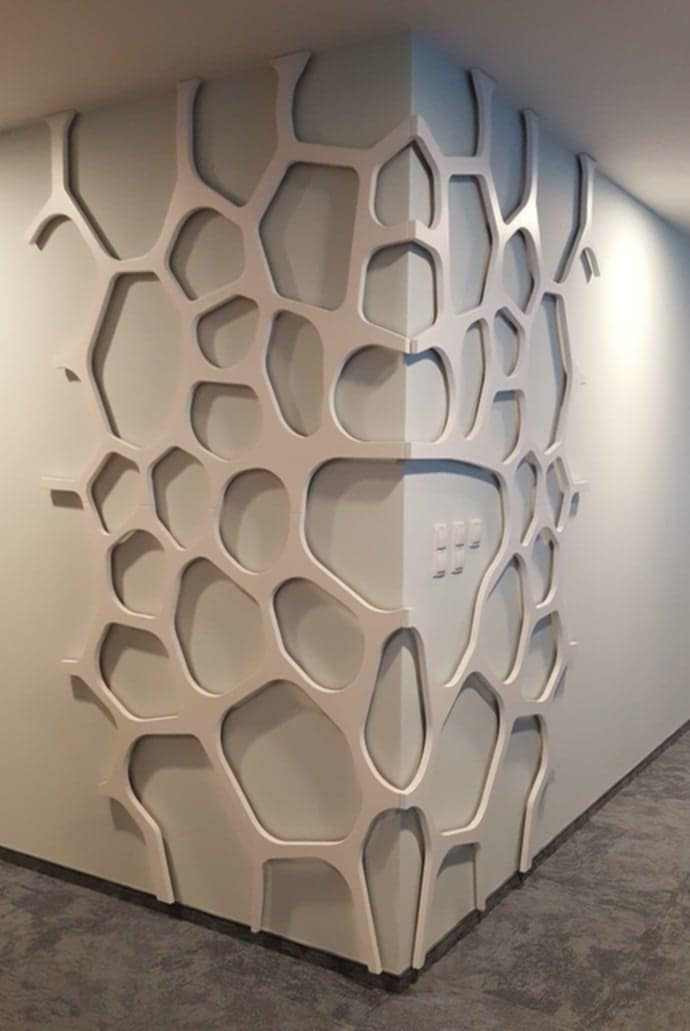 Abstrakcyjna, beżowa dekoracja ścienna w kształcie organicznej siatki, pokrywająca narożnik pokoju z widocznymi włącznikami światła. Nowoczesny design.