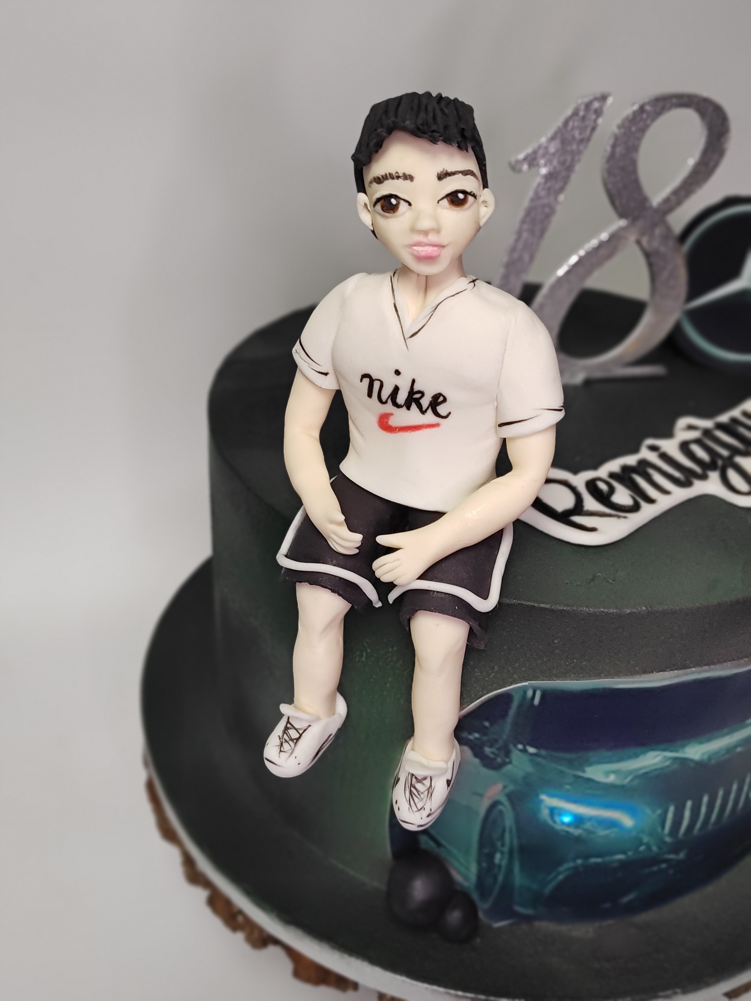 Tort urodzinowy z figurką chłopca w sportowym stroju, logo Nike i motywem samochodu Mercedes. Dekoracja na osiemnaste urodziny, srebrna liczba 18.