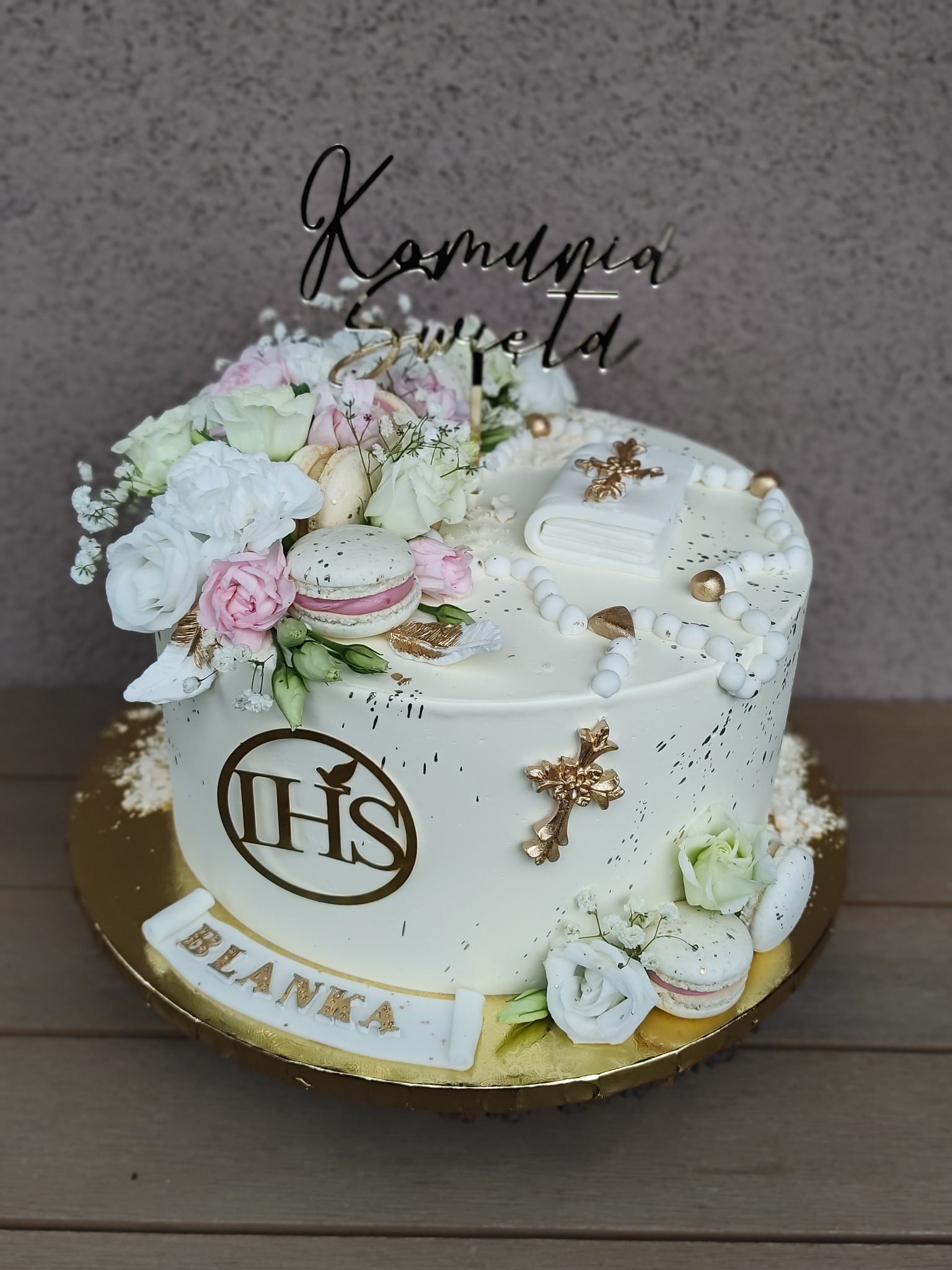 Tort komunijny z napisem 'Komunia Święta', kwiatami, makaronikami i symbolami religijnymi, umieszczony na złotej paterze. Dekoracja dla dziewczynki o imieniu Blanka.