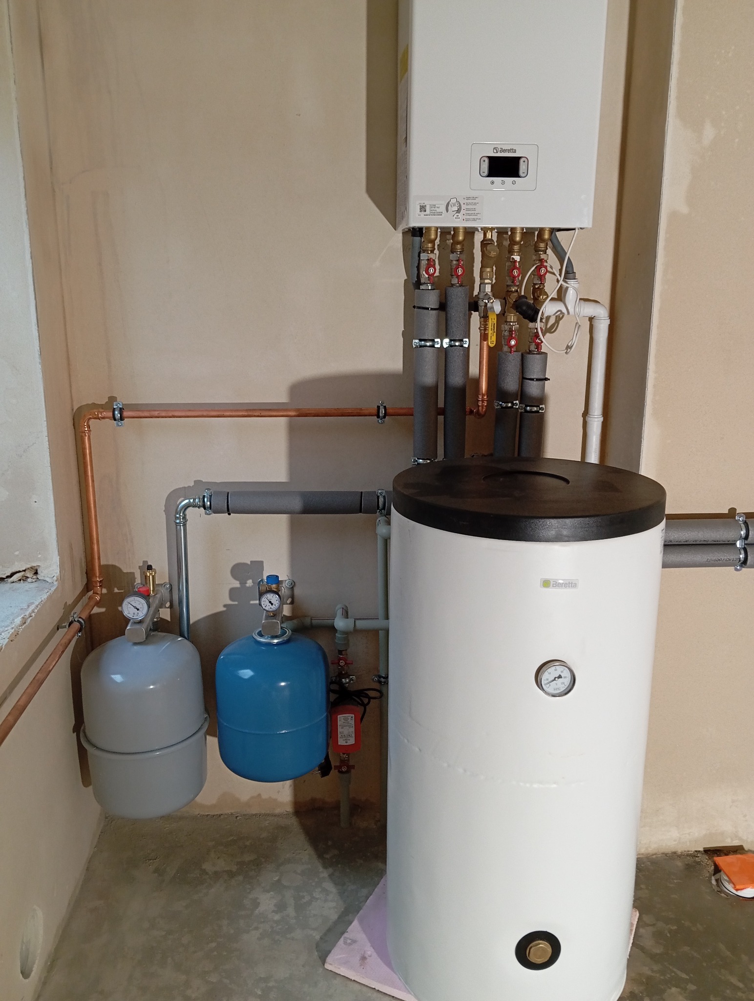 Kompaktowa instalacja grzewcza Beretta z widocznym zasobnikiem ciepłej wody i naczyniami przeponowymi w pomieszczeniu o surowym wykończeniu ścian.