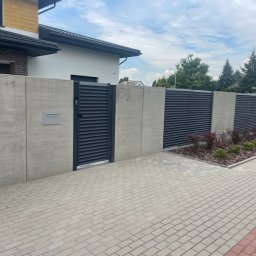Energo Usługi Spawalnicze GRZEGORZ GODULA - Nowoczesne ogrodzenie z szarych, poziomych paneli i betonowych słupków, brama wejściowa z numerem domu '81', skrzynka pocztowa, kostka brukowa.