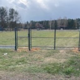 Energo Usługi Spawalnicze GRZEGORZ GODULA - Nowoczesne ogrodzenie panelowe z bramą wjazdową na posesji, widok z poziomu gruntu, z fragmentem drzewa w kadrze i budynkiem w tle.