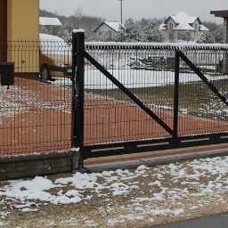 Energo Usługi Spawalnicze GRZEGORZ GODULA - Nowoczesna, czarna brama przesuwna i furtka z paneli ogrodzeniowych na posesji w zimowej scenerii. Elementy konstrukcyjne pokryte śniegiem.