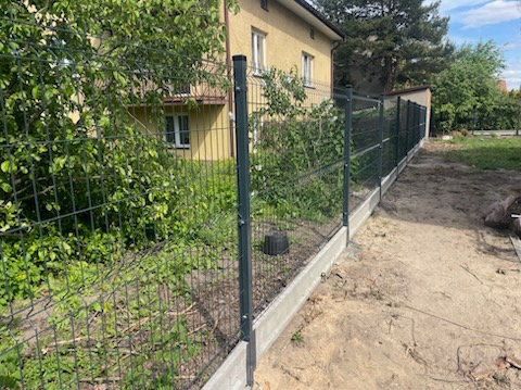 Nowoczesne ogrodzenie panelowe z podmurówką betonową, widok z perspektywy ziemi, zieleń w tle. Charakterystyczne mocowania paneli.