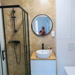 REMONT SPEC Bogdan Kondzior - Nowoczesna łazienka z kabiną prysznicową typu walk-in, umywalką nablatową i lustrem w czarnej ramie. Ściany wyłożone płytkami w jodełkę.