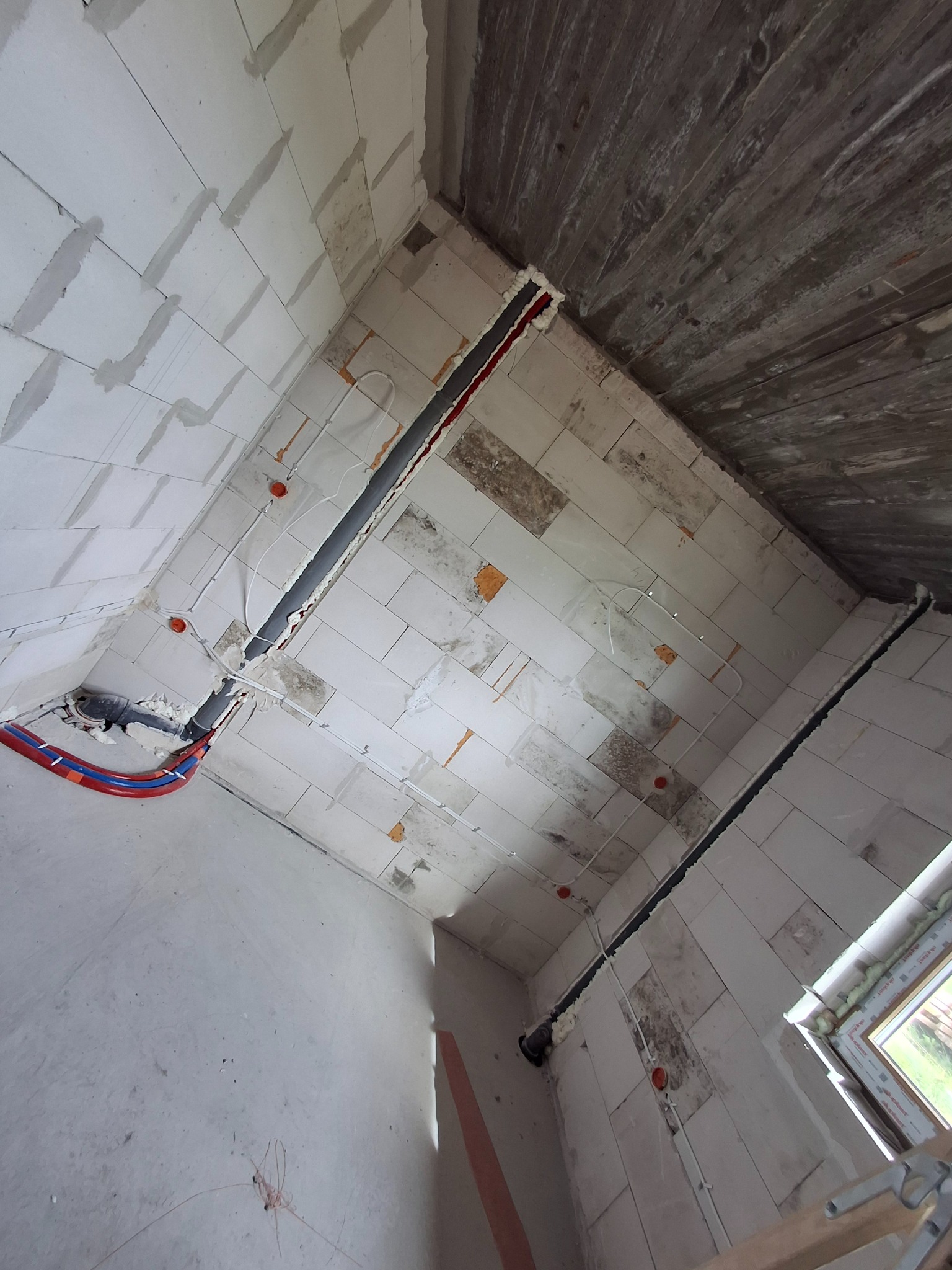 Wnętrze w trakcie prac instalacyjnych: widoczne rury grzewcze, przewody elektryczne, puszki instalacyjne w ścianach z betonu komórkowego i surowym stropem.