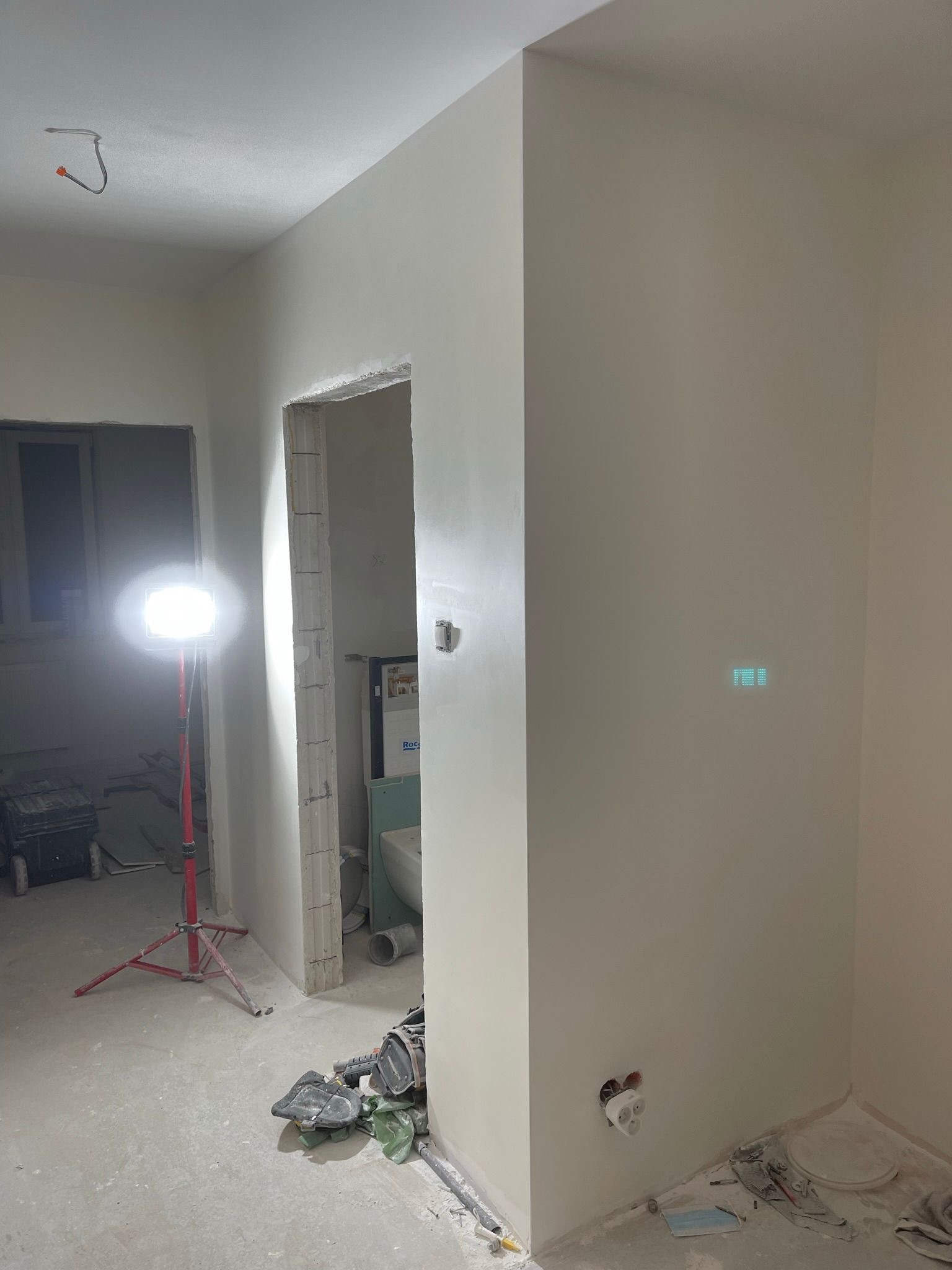 Wnętrze po szpachlowaniu: gładkie, białe ściany, widoczne narzędzia i lampa budowlana. Przygotowanie do malowania w trakcie remontu łazienki.