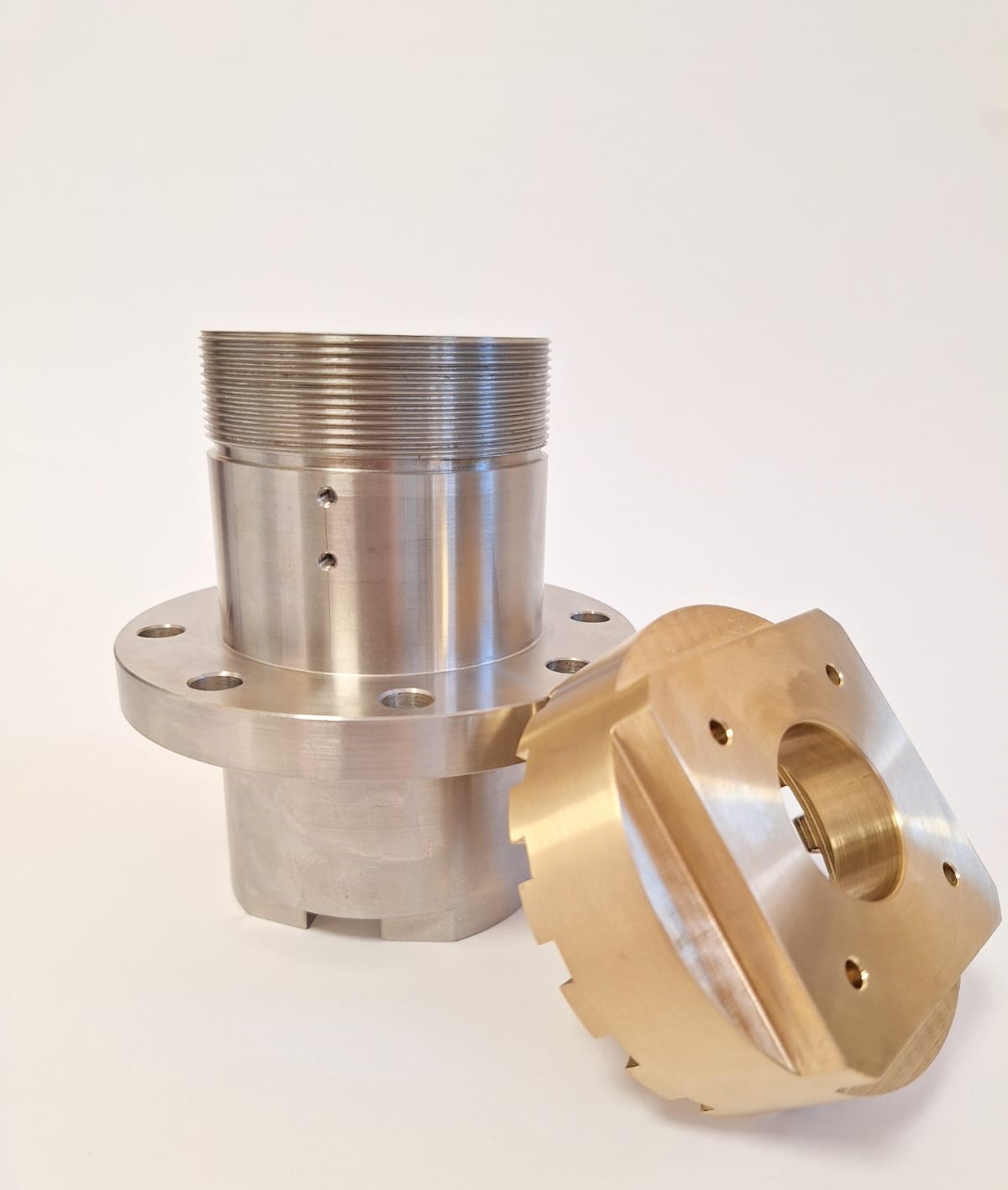 Precyzyjnie wykonane, metalowe elementy: srebrny cylinder z gwintem i kołnierzem oraz złoty, kwadratowy element z wycięciami, oba z otworami na śruby. Gładkie powierzchnie, ostre krawędzie.