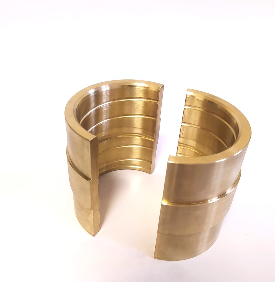 Dwie połówki mosiężnego elementu cylindrycznego z wyżłobieniami, rozdzielone, na białym tle. Precyzyjna obróbka metalu, widoczne ślady toczenia.