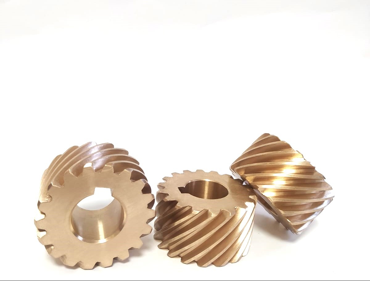 Trzy precyzyjnie wykonane, spiralne koła zębate z brązu na białym tle. Widoczne detale obróbki, centralne otwory i ukośne ząbkowanie.