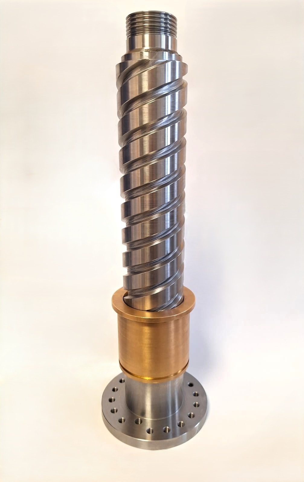 Precyzyjnie wykonana śruba trapezowa ze stali nierdzewnej z gwintem śrubowym i mosiężną nakrętką, stojąca pionowo na białym tle. Widoczne otwory montażowe.