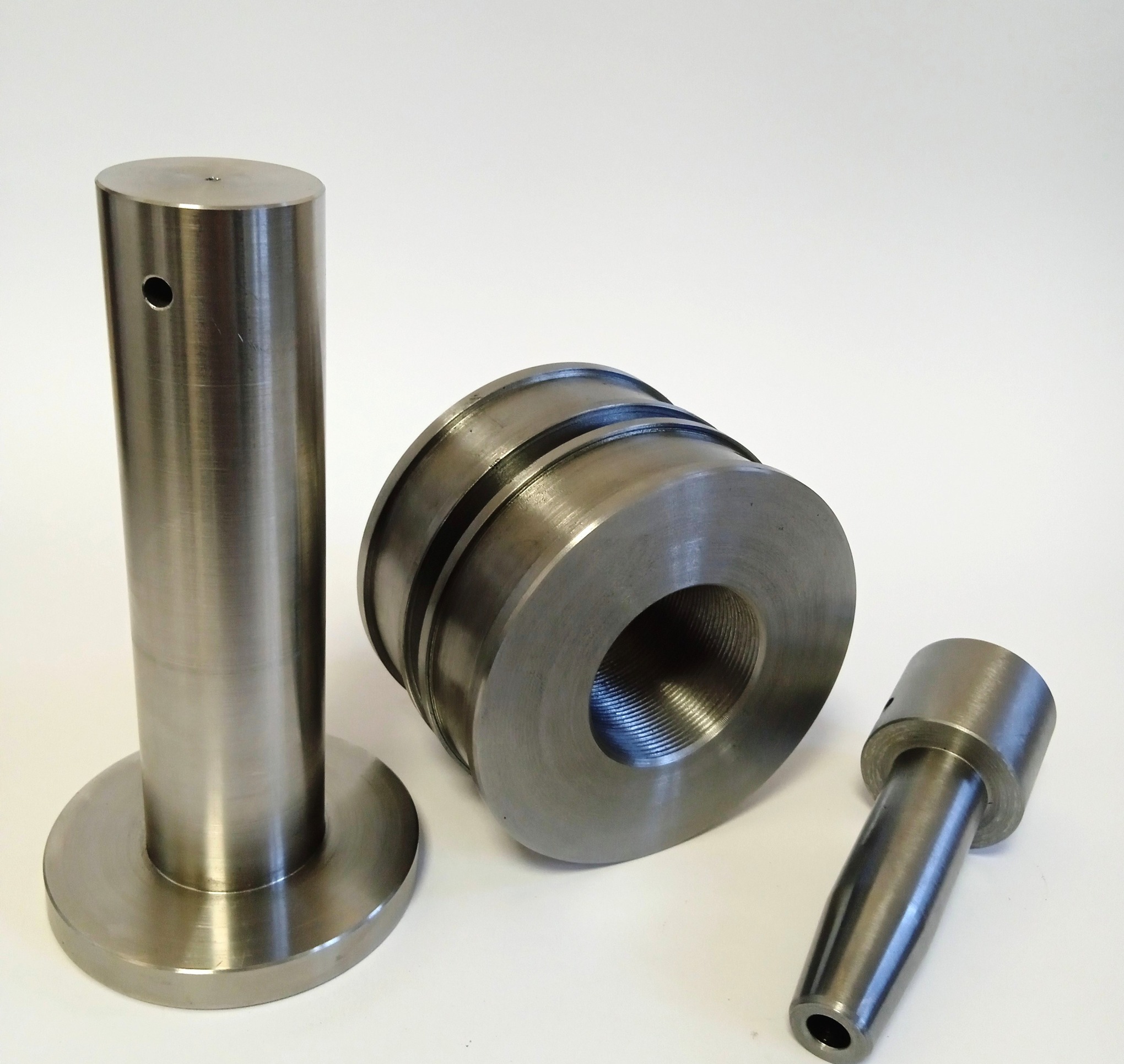 Precyzyjnie wykonane, metalowe elementy obrabiane, widoczne gwinty, otwory i ślady obróbki. Detale na białym tle, ukazujące dokładność wykonania.