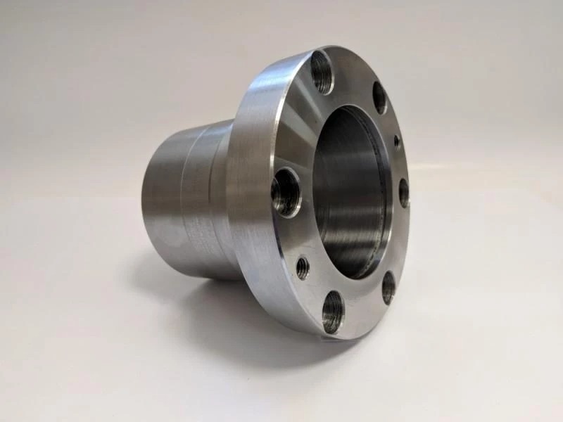 Precyzyjnie wykonany, metalowy element z widocznymi otworami, prawdopodobnie flansza, obrobiony z dużą dokładnością, leżący na jasnym tle.