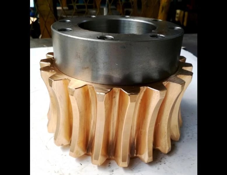 Precyzyjnie wykonana, brązowa przekładnia ślimakowa z metalowym pierścieniem, widoczna na blacie roboczym. Detal obróbki metali, bliski kadr.