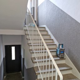 Sch 04 remonty - Klatka schodowa po malowaniu: białe ściany, szary tynk strukturalny na ścianie bocznej. Na schodach radio budowlane Makita. Widok z dołu, w tle czarne drzwi.