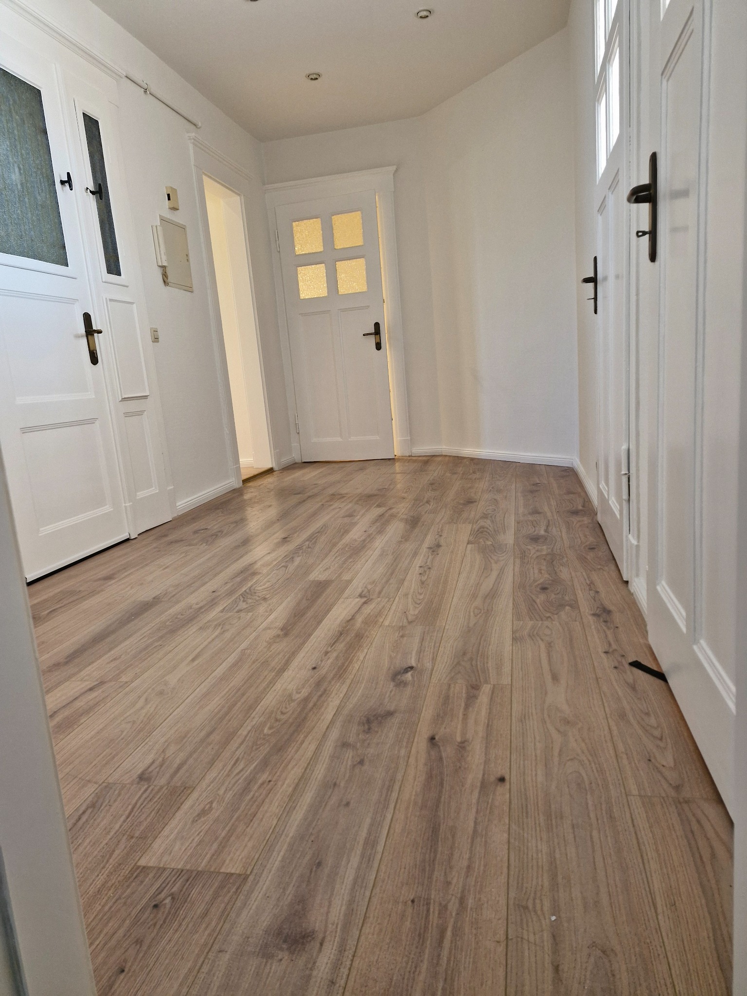 Jasne panele podłogowe w korytarzu z białymi drzwiami i ścianami. Widok na wprost, ukazujący wzór drewna i czystość wykonania.