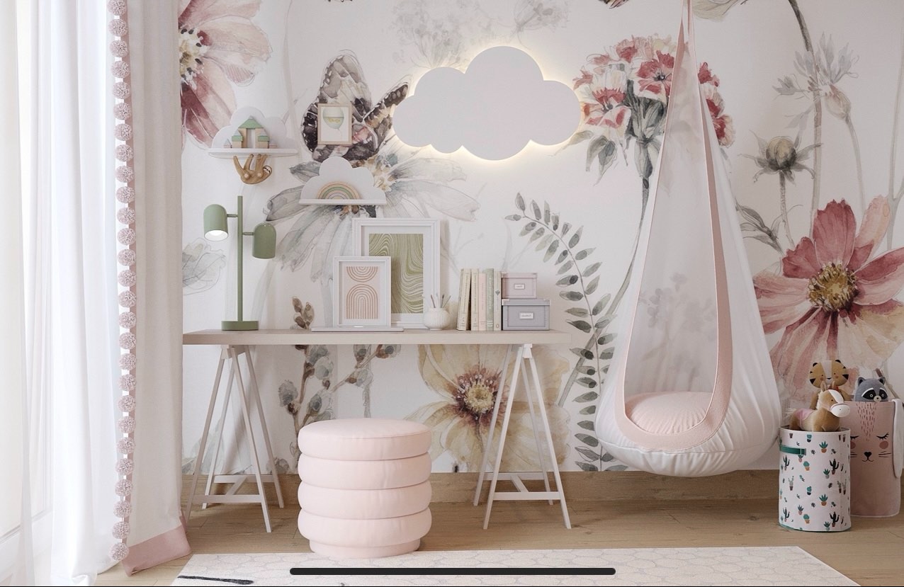 Pokój dziecięcy z biurkiem, lampką, pufą i wiszącym fotelem, w pastelowych barwach, z tapetą w kwiaty i motyla oraz podświetlaną chmurką na ścianie.