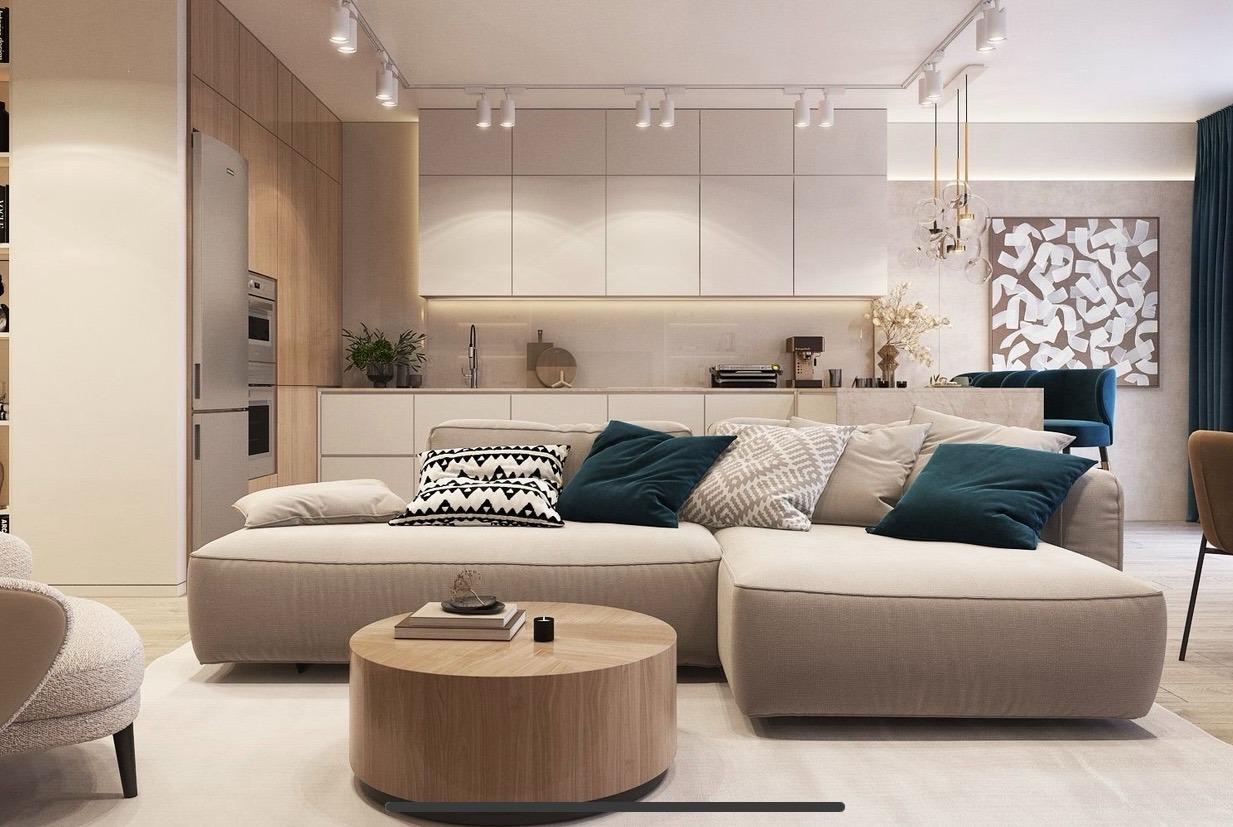 Stylowe wnętrze salonu z aneksem kuchennym w Warszawie. Beżowa sofa z poduszkami, okrągły stolik kawowy, nowoczesne oświetlenie i minimalistyczna zabudowa kuchenna.