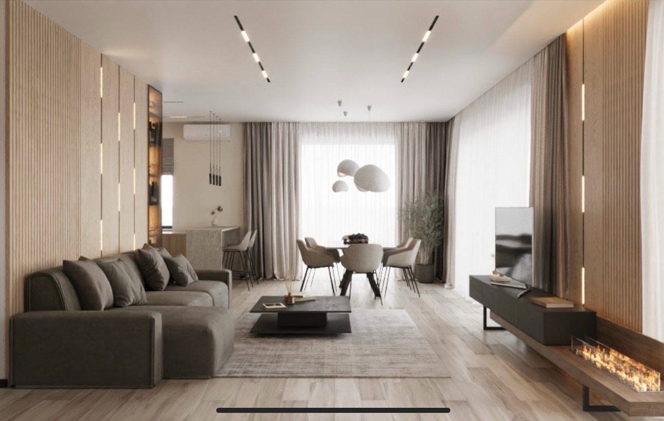 Wnętrze salonu z jadalnią w odcieniach beżu i szarości. Sofa, stół z krzesłami, telewizor i kominek tworzą spójną całość. Minimalistyczne oświetlenie i drewniane panele ścienne.