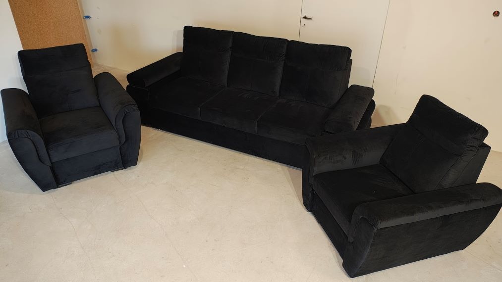 Komplet mebli tapicerowanych: sofa trzyosobowa i dwa fotele w czarnym welurze. Klasyczny design, wysokie oparcia, komfortowe siedziska. Ustawione w jasnym wnętrzu.