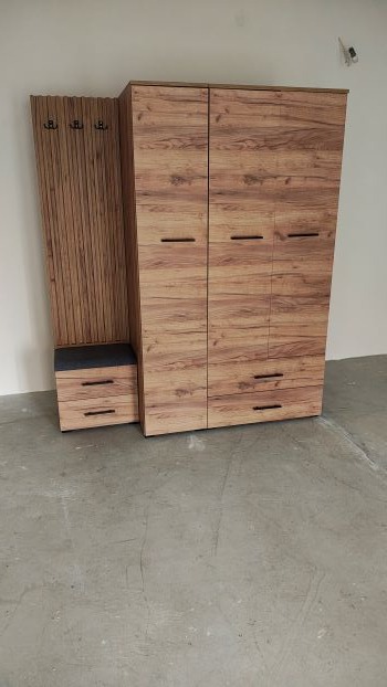 Komplet szafy z siedziskiem i wieszakami w odcieniach brązu, imitacja drewna. Szafa trzydrzwiowa z szufladami, minimalistyczne uchwyty, szary beton na podłodze.