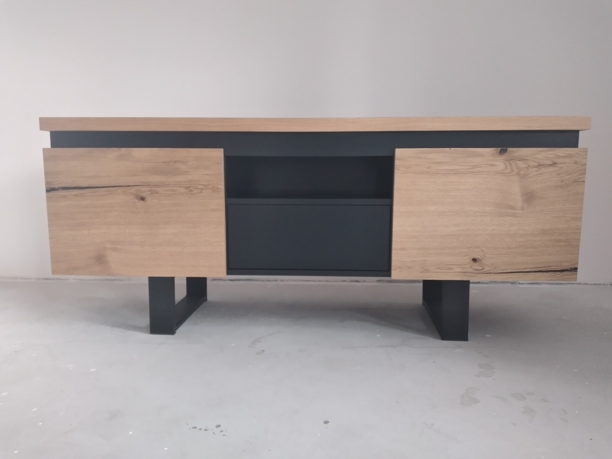 Nowoczesna komoda RTV z drewnianymi frontami i grafitowym korpusem na metalowych nogach. Minimalistyczny design, naturalne materiały, widoczna struktura drewna.