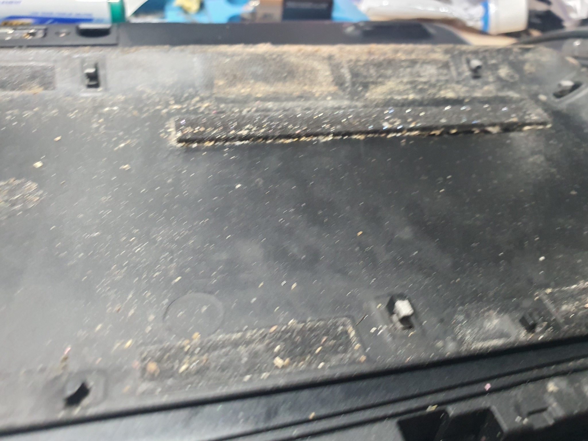 Zanieczyszczona, czarna obudowa laptopa z widocznymi śladami kurzu i okruchów, wymagająca czyszczenia. Detal naprawy sprzętu komputerowego.