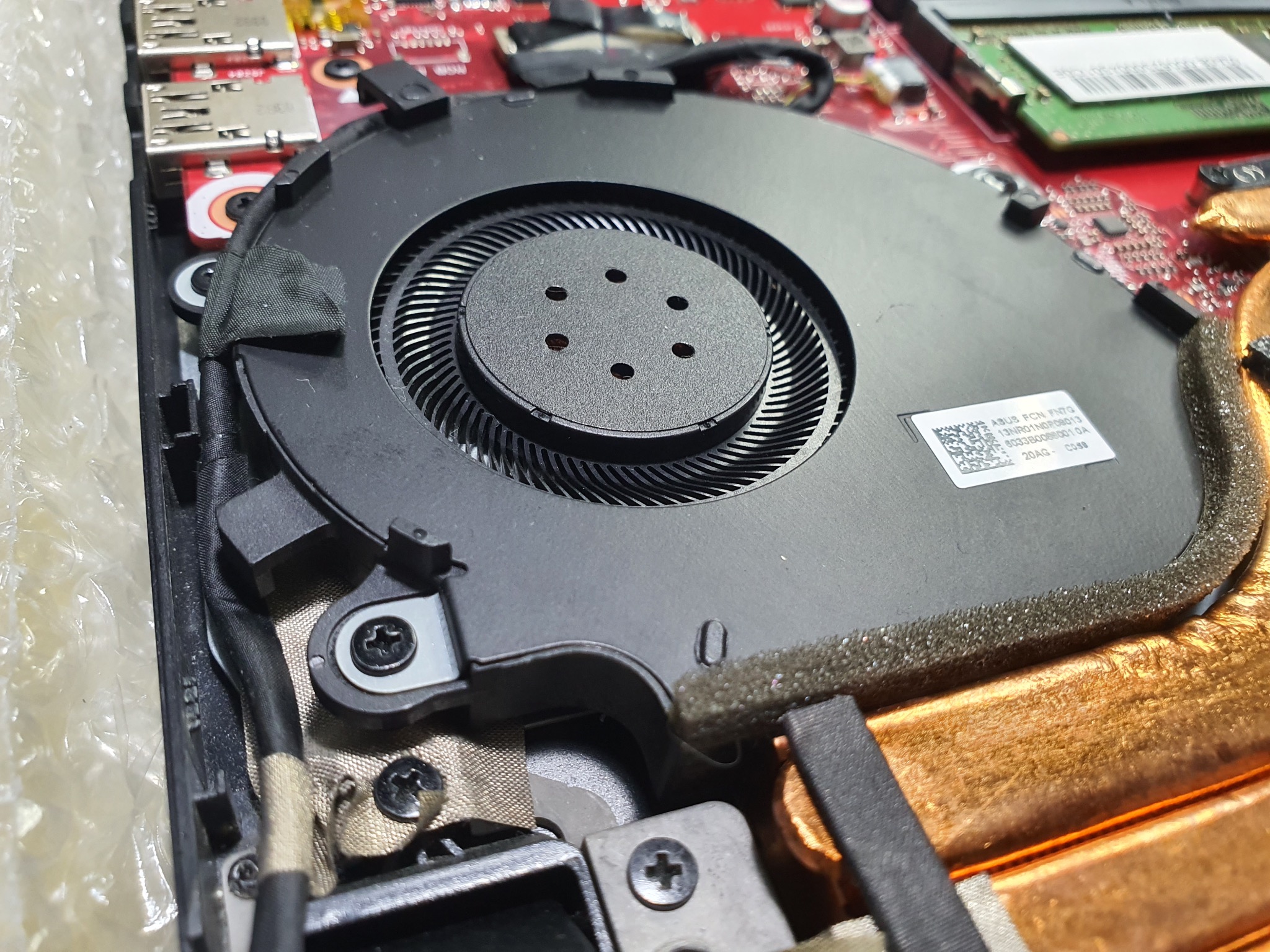 Wnętrze laptopa: czarny wentylator z radiatorem, widoczne śrubki, kable i elementy płyty głównej. Detaliczny widok na system chłodzenia w trakcie serwisu.