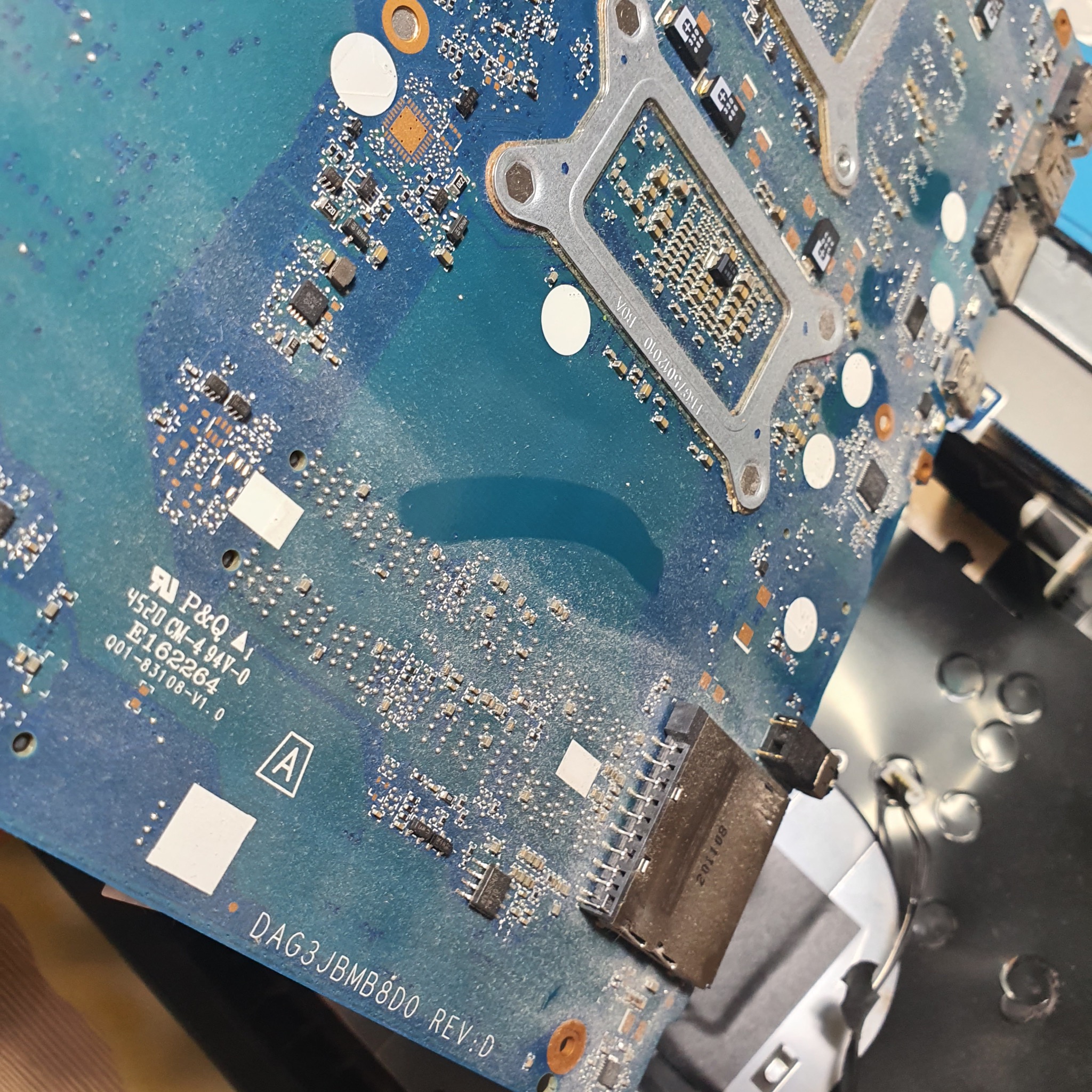 Płyta główna laptopa w zbliżeniu, widoczne układy scalone, złącza i oznaczenia. Detaliczna prezentacja elektroniki podczas naprawy.