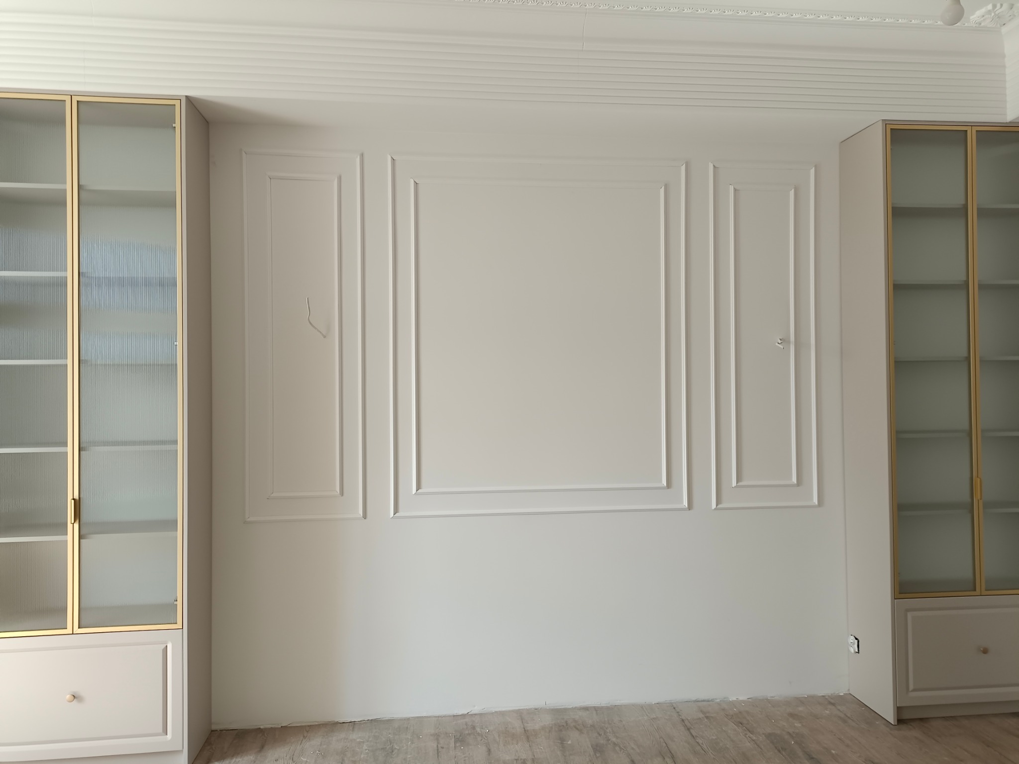 Eleganckie wykończenie wnętrza: kremowe ściany z dekoracyjnymi listwami i symetrycznie ustawione przeszklone witryny z złotymi ramkami.