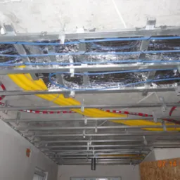 Sufit podwieszany w trakcie montażu z widocznymi kablami w peszlach (żółte, czerwone) oraz niebieskimi przewodami, zabezpieczonymi folią aluminiową.